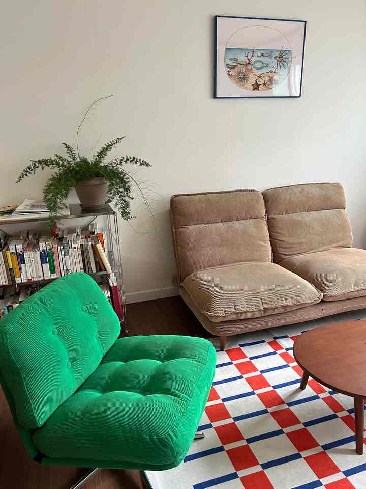 ナチュラルな色調のリビング、ベージュのソファと緑のアームチェア、チェック柄ラグが配置された印象的なインテリア