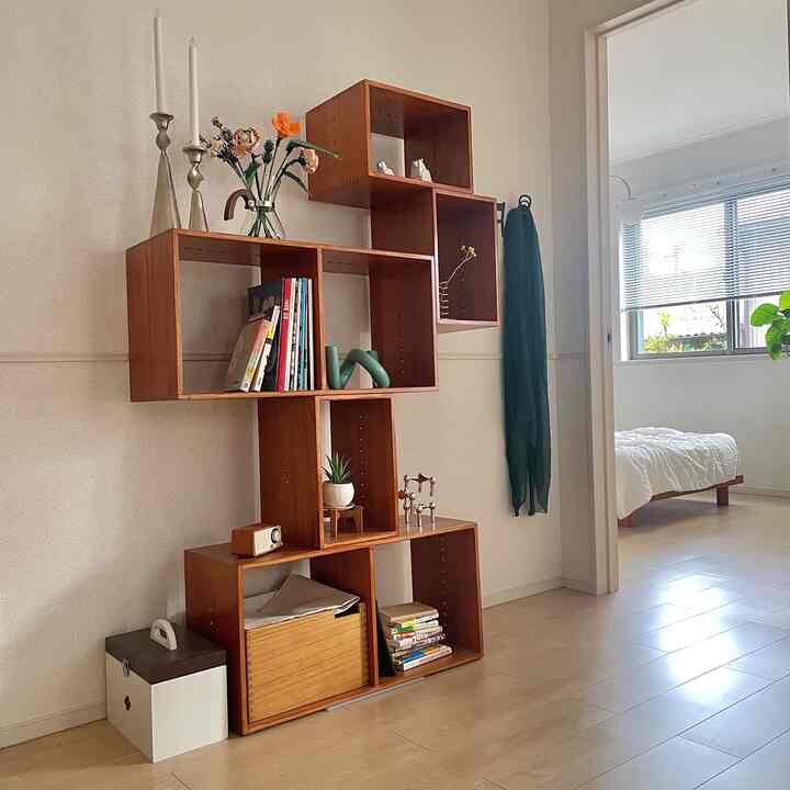 White and beige toned studio apartment living room featuring a mid-century modern wooden bookshelf with a cozy atmosphere