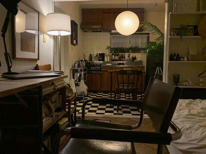 白と木目調が調和した狭いワンルーム、暖かいフロアランプの灯りがある雰囲気のある台所と寝室の空間