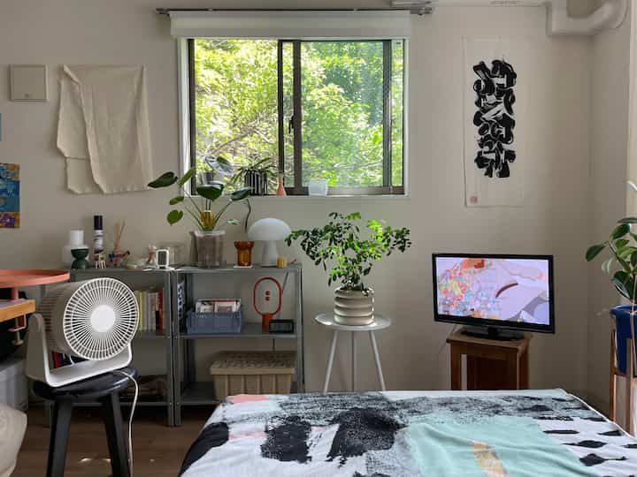 White and brown toned 1K bedroom featuring leafy plants by the window and a table lamp in a natural atmosphere