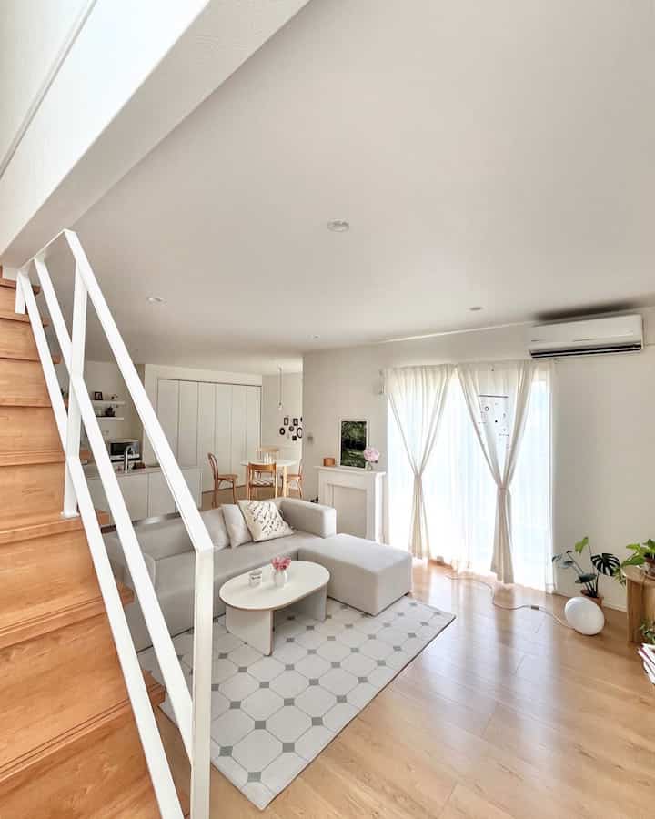 白と木目調が調和した階段とリビング、ソファとコーヒーテーブルが配置されたナチュラルモダンな空間