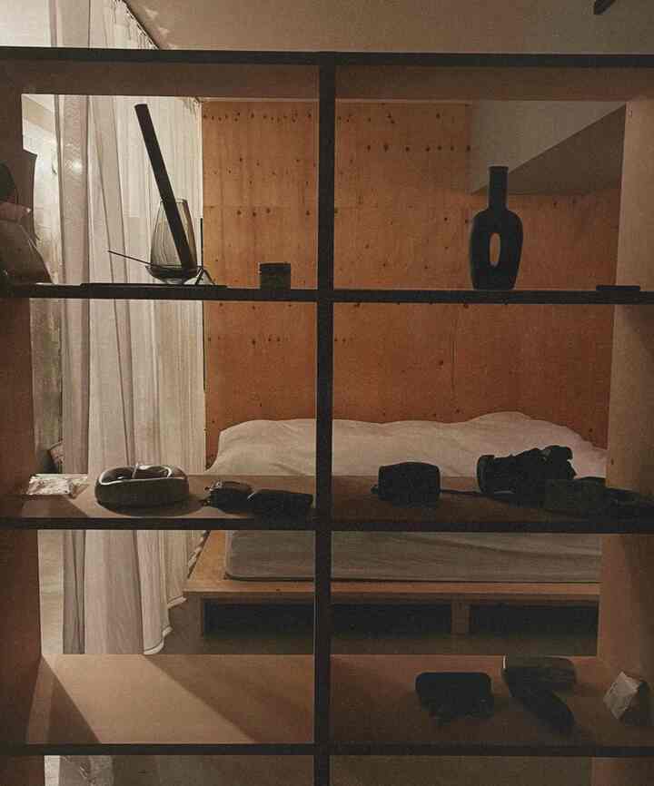 Studio apartment bedroom with brown wood tones and white bedding, featuring simple natural shelving creating a cozy atmosphere