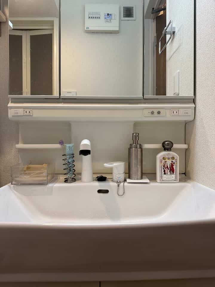 白を基調とした狭くシンプルなバスルームの洗面台、鏡と整理された日用品が配置された雰囲気のあるインテリア