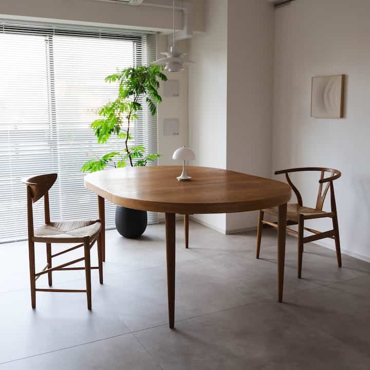 Natural tone dining room featuring wooden table and chairs with a tall plant near large window for a cozy atmosphere
