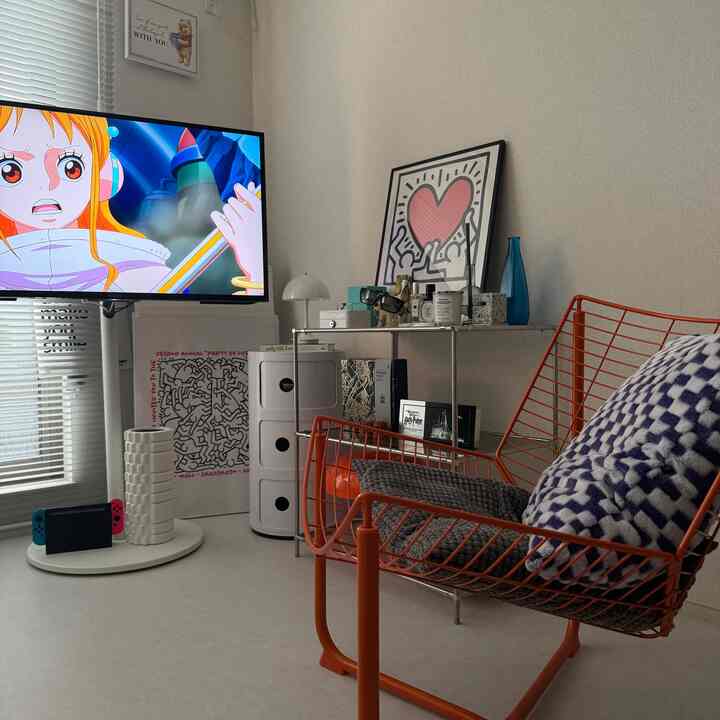 白を基調とした韓国インテリアのリビング、オレンジのワイヤーチェアとテレビ、シンプルで雰囲気のある空間