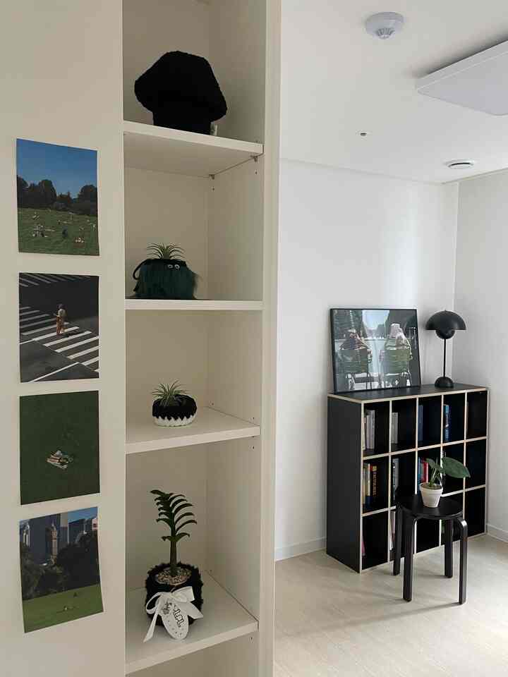 白い壁と棚、黒い本棚とスツール、植物が配置されたミニマルな書斎の雰囲気あるインテリア