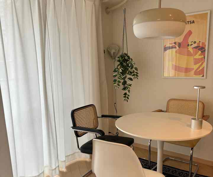 A cozy small dining room in white and brown tones featuring rattan dining chairs and a round table