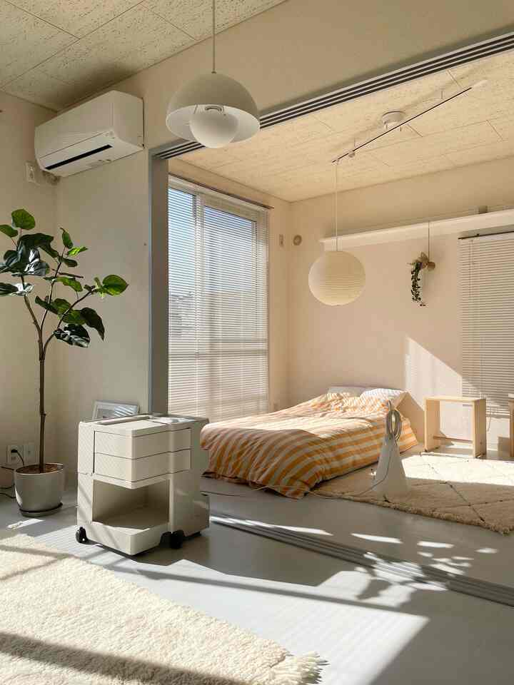 白とベージュのトーンのワンルーム寝室、ボビーワゴンと木製家具が配置された自然な雰囲気のインテリア