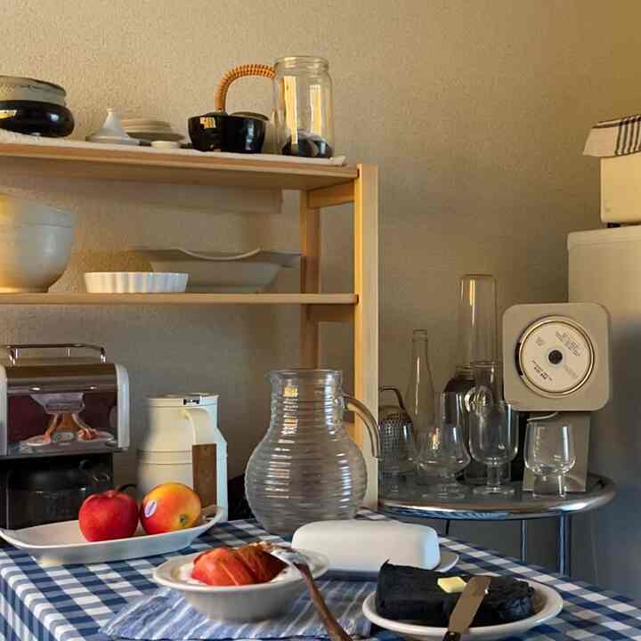 アイボリー色の壁とブラウンの木製棚があるキッチン、チェック柄のテーブルクロスに果物や調理器具が配置された雰囲気のあるインテリア