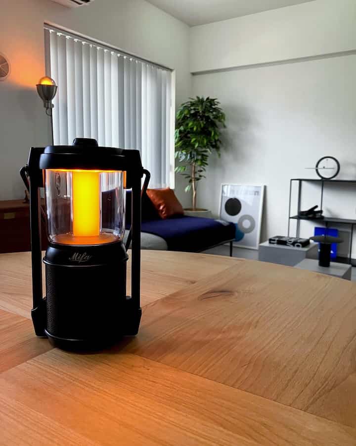 白い壁と木目調のテーブルがあるリビング、ネイビーのソファと黒のランタンスピーカーが配置された洗練された空間