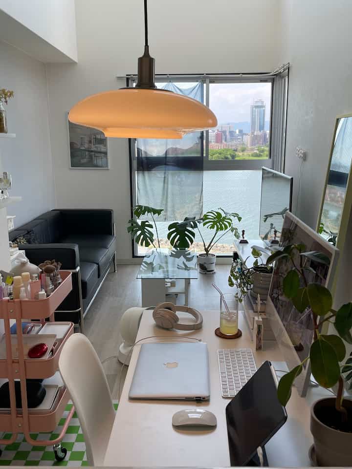 白を基調としたワンルームリビング、黒いソファと植物、大きな窓と作業スペースがある雰囲気のあるインテリア