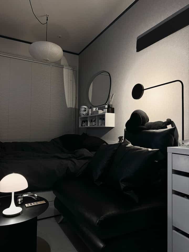 ダークグレーとブラックトーンの寝室、ブラックレザーソファと壁照明が配置されたモダンで雰囲気のあるインテリア