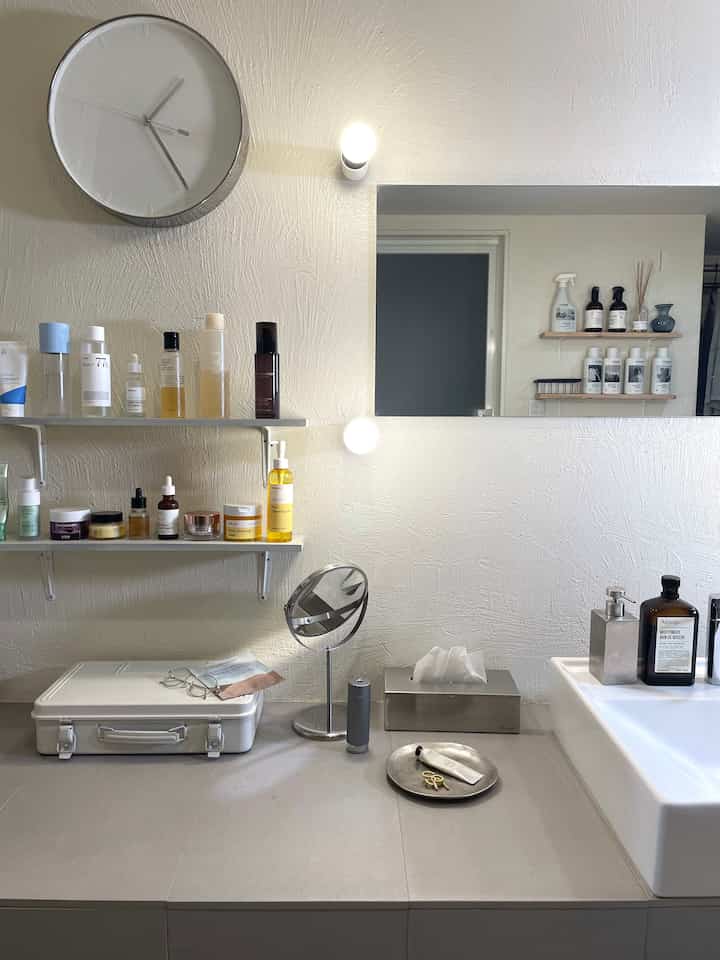 白とベージュのトーンのバスルーム、壁の棚にスキンケア製品が整然と並ぶシンプルで清潔感あるインテリア