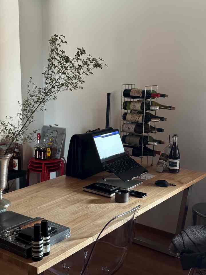 Natural wood-toned studio apartment home office featuring a wine rack, transparent stool, and plant in a tidy living room space