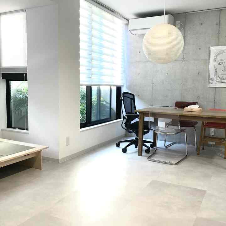 Bright gray-toned dining room with exposed concrete wall, featuring transparent chair and spherical pendant light in a modern natural space