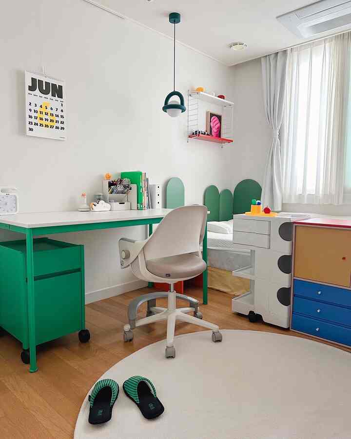 白と緑のトーンの寝室兼書斎、整ったデスクとオフィスチェア、丸いラグが配置された落ち着いた空間