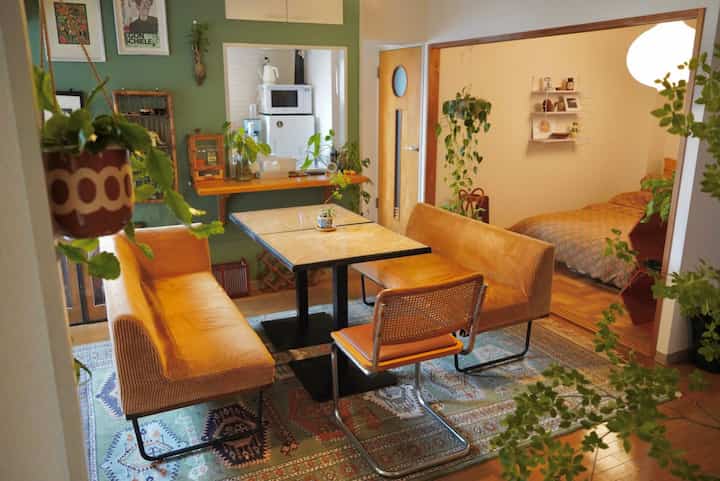 Natural wood-toned living and dining area designed for two people featuring vintage rug, cozy sofas, and abundant plants