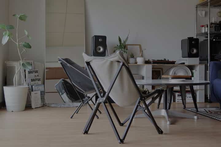 白とナチュラルカラーのリビング、アウトドアチェアとローテーブル、コンクリートブロックの棚が配置されたシンプルなインテリア