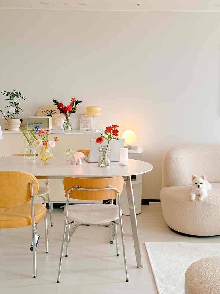 白とベージュの色調のリビング、中央に白い楕円形のダイニングテーブルと異なる色の椅子が配置された自然な雰囲気のあるインテリア