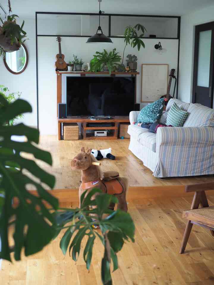 ウッドトーンの床と白い壁のリビング、子供用の乗り物の馬とソファが配置された温かみのある空間