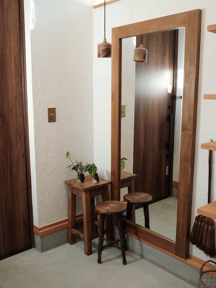 Natural wood tone and white-walled compact entrance featuring a large wood-framed mirror and two wooden stools