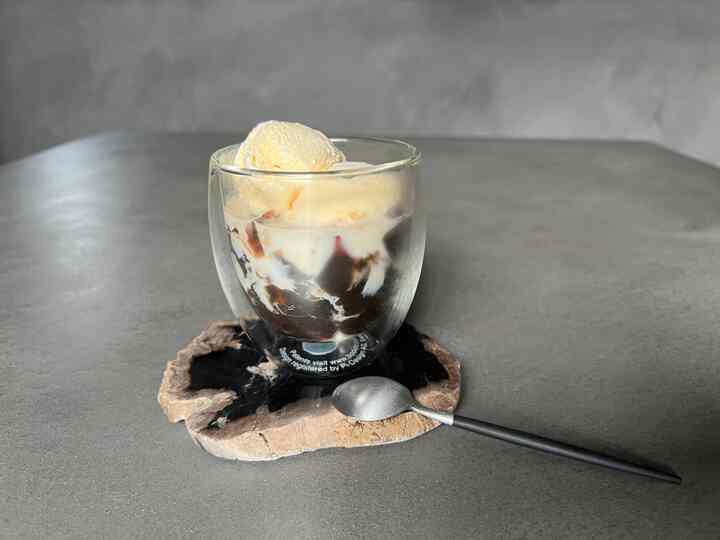 グレー調のモダンな空間、モールテックスのテーブルの上に自然石のコースターとガラスのカップが配置されたおうちカフェの雰囲気あるインテリア