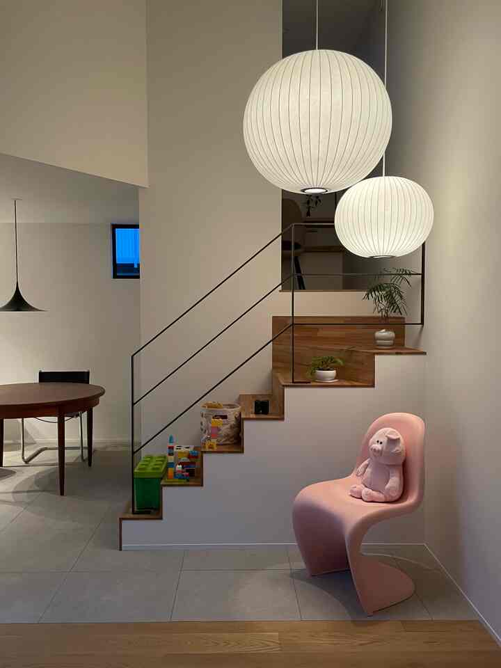 A modern and clean dining area featuring stairs in white and wood tones, a pink pendant chair, and children's toys beside the stairs