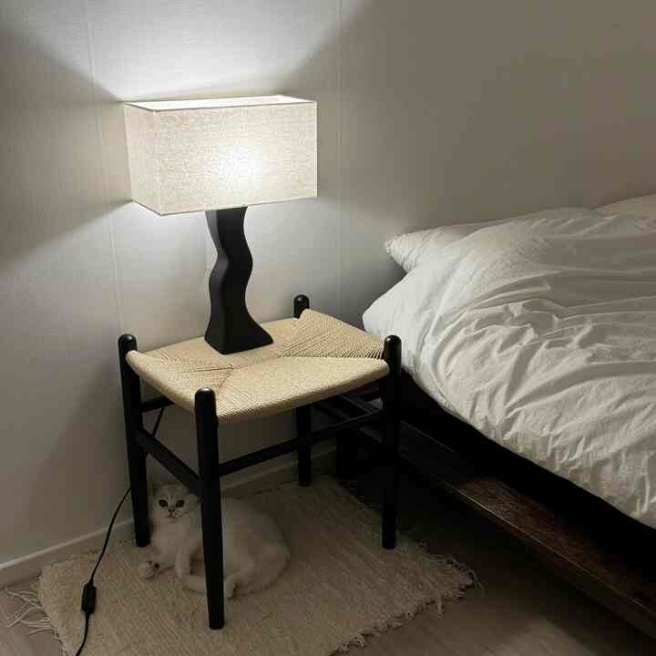 ホワイトとブラックのトーンの寝室、ラタン製スツールとアクセントライトが配置されたミニマルな空間