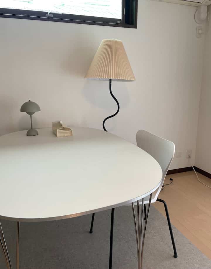 白いダイニングテーブルと椅子が配置されたダイニングルーム、木目調の床とフレンチカントリースタイルのフロアランプがあり、シンプルでモダンな雰囲気のインテリア