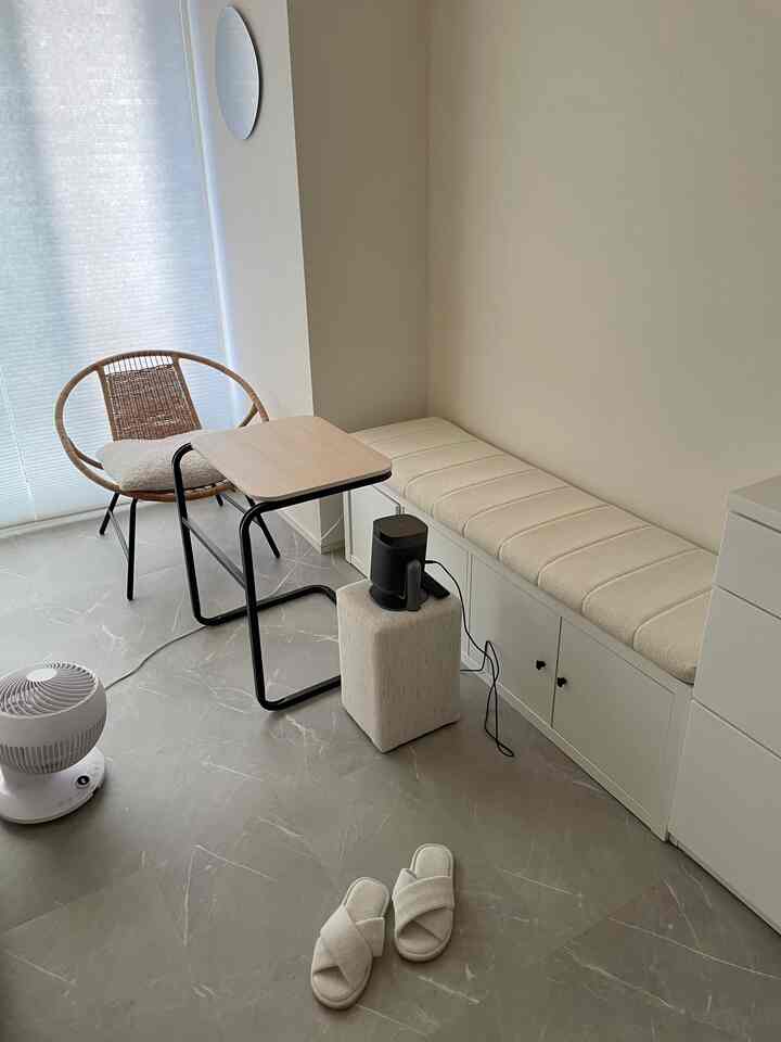 白とグレーのトーンの小さな部屋、ラタンチェアと収納ベンチ、サイドテーブルが配置されたシンプルでモダンな空間