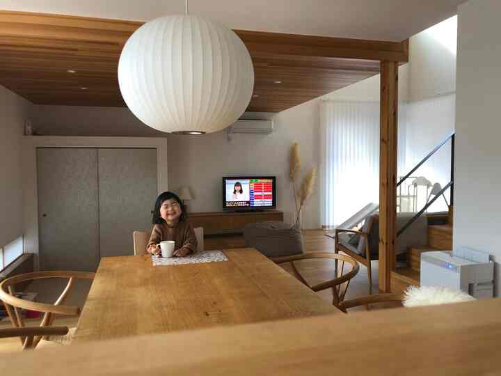 木目調とベージュの調和がとれたナチュラルなリビングダイニング、中央にダイニングテーブルと笑顔の子供が配置された温かみのある空間