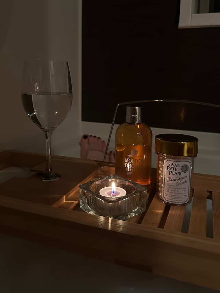 木目調と白が調和したバスルームのバストレイにキャンドルとバスジェルが置かれた落ち着いた雰囲気の空間