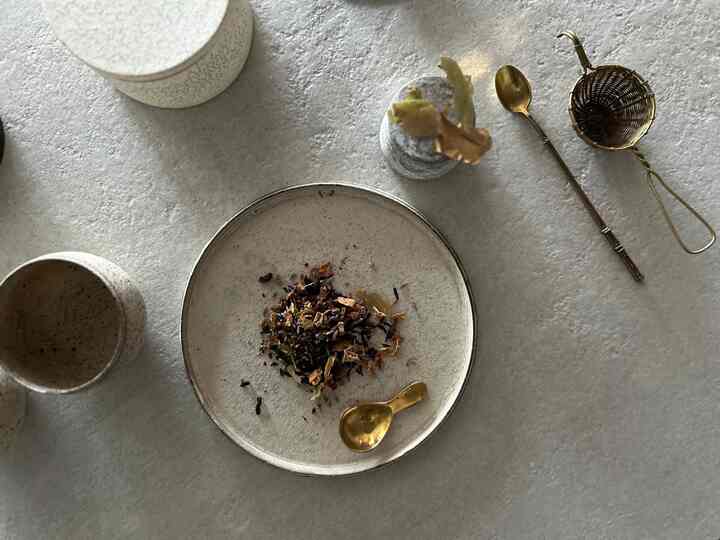 アイボリーの皿とゴールドのティースプーン、ティーストレーナーが置かれたミニマルなテーブル上のティーセット