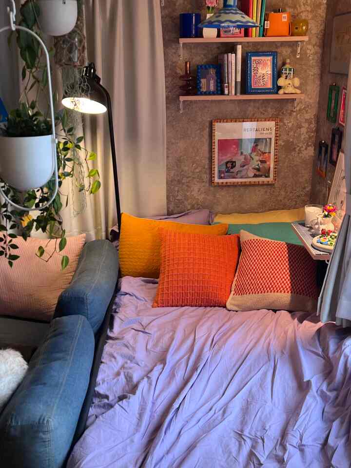 ラベンダーカラーの寝室、多彩なクッションとソファ、フロアランプが配置された雰囲気のある空間