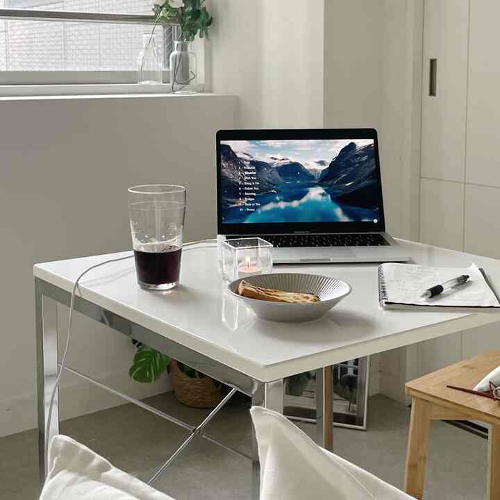 白とグレーのモノトーンが基調の1人暮らし1K空間、整ったダイニングテーブルにノートパソコンと飲み物が配された雰囲気のあるインテリア