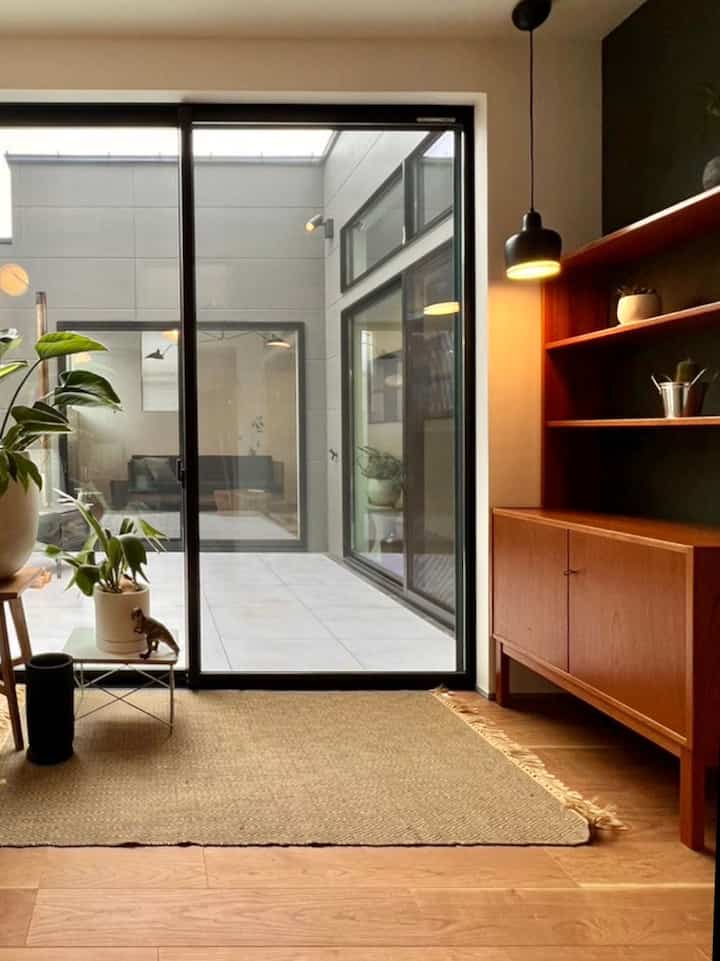 ベージュと木目調の調和が美しい玄関兼サンルーム、植物とヴィンテージ家具が配置された自然な雰囲気の空間