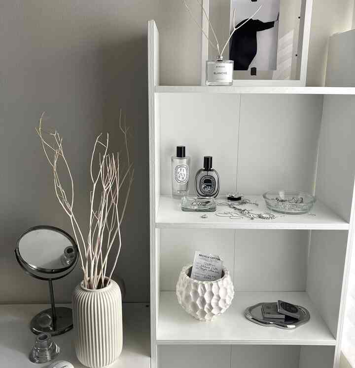 Minimalistic white and gray interior featuring a clean shelf with vase, perfumes, and picture frame