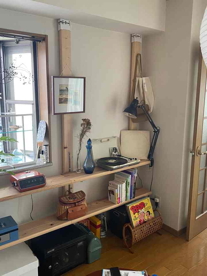Natural-toned small studio apartment featuring wooden bookshelf with books, vinyl player, and retro clock creating cozy vibe