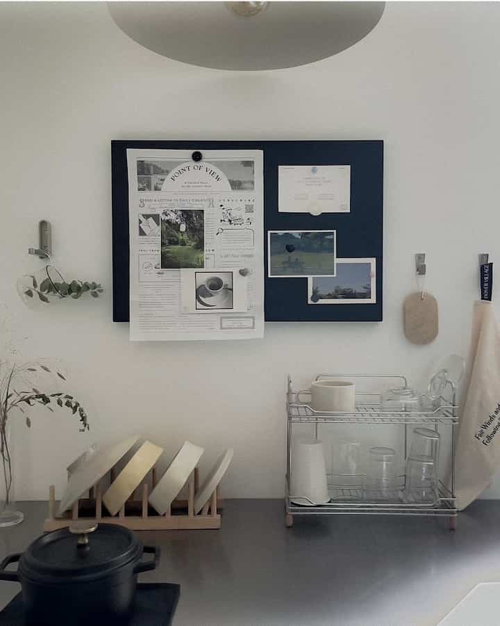 白い壁とネイビーカラーの掲示板があるキッチン、整然と並べられた皿とカップが印象的なモダンでミニマルなインテリア