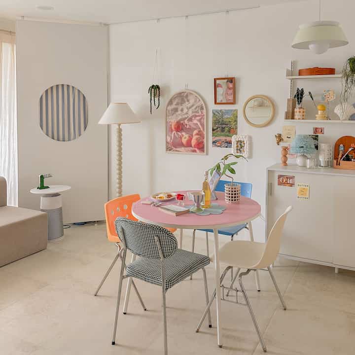 明るく爽やかなホワイトトーンのリビング、ピンクの丸いダイニングテーブルとカラフルな椅子が配置された雰囲気のあるホームカフェ空間