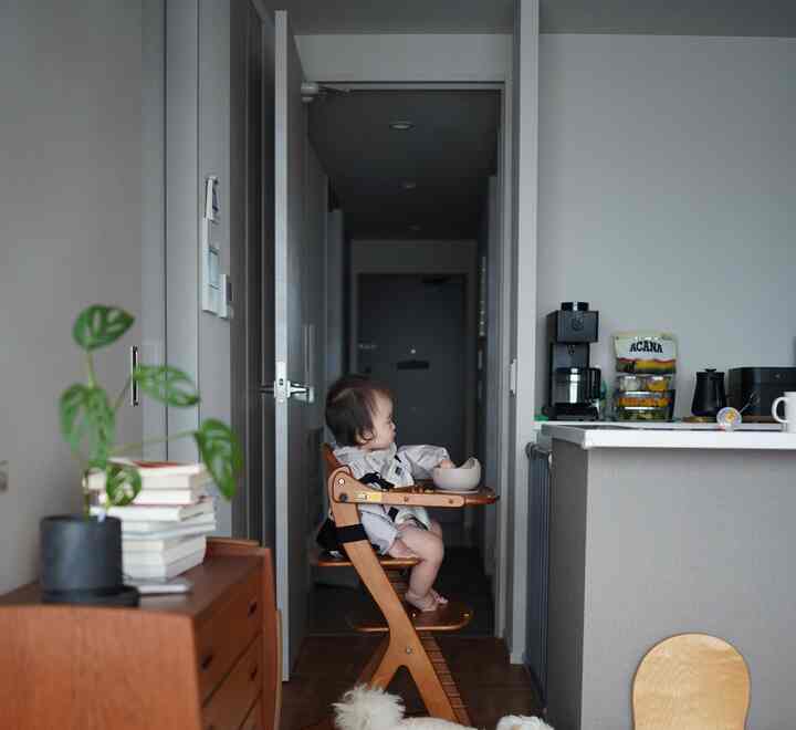 ナチュラルな木目調とグレーの色調が調和するキッチン空間、ハイチェアに座る赤ちゃんと床で食事する犬がいる温かみのあるインテリア