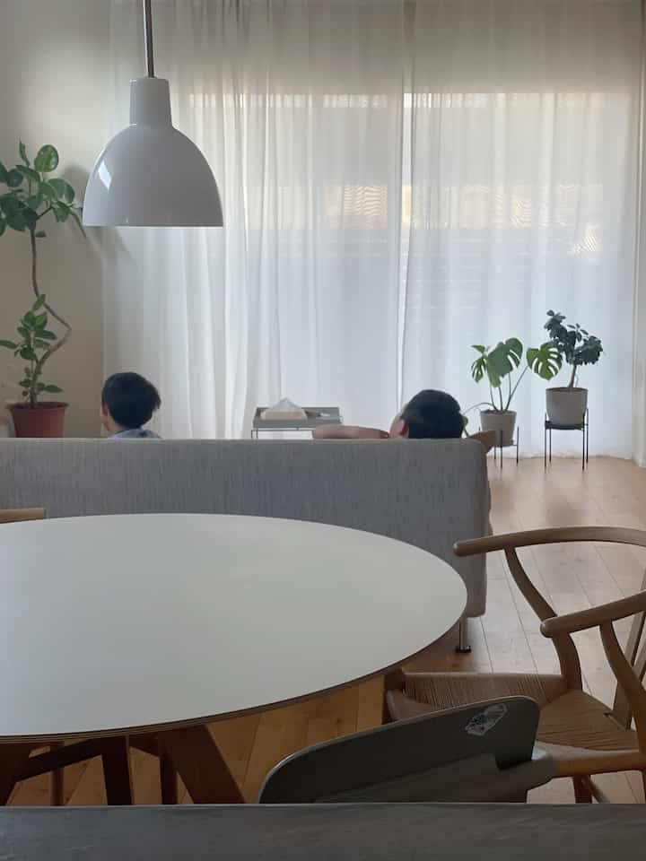 A living room with white curtains and natural-colored furniture featuring children sitting on the sofa, creating a calm atmosphere