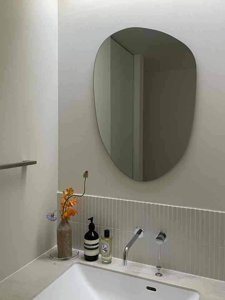 明るいホワイトトーンのバスルーム洗面台エリア、花の入ったガラスの花瓶、高級なハンドウォッシュとルームスプレーが配置された、清潔で自然な雰囲気のインテリア