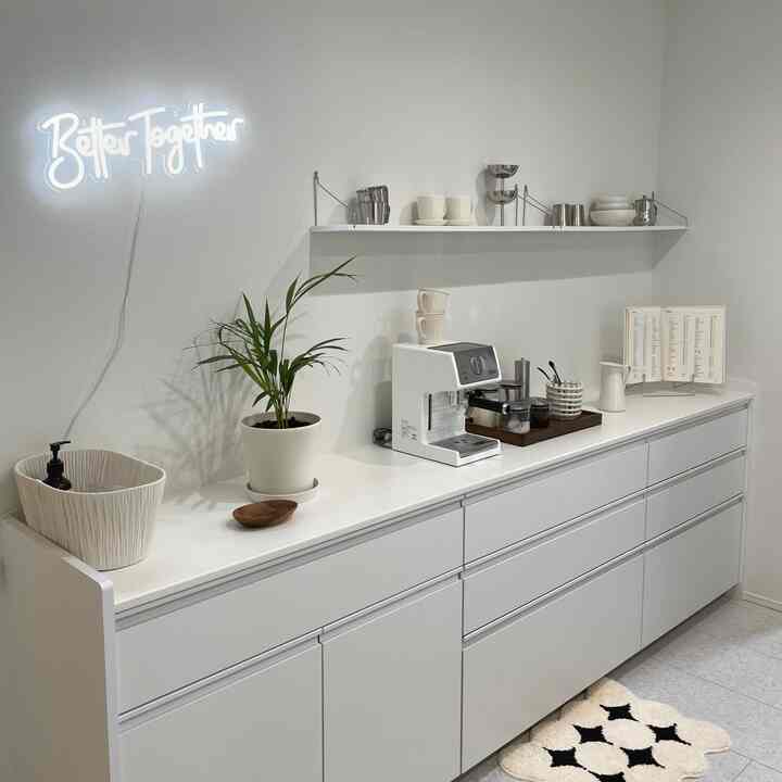 清潔感のある白を基調としたキッチン、キャビネットの上にコーヒーメーカーと植物が置かれ、落ち着いたおうちカフェの雰囲気