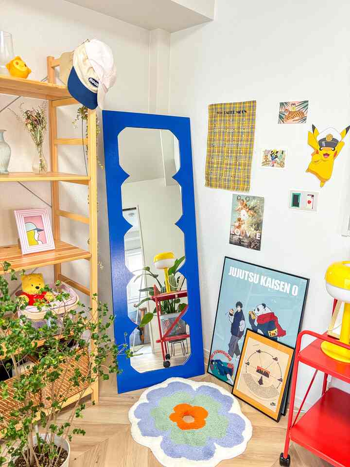 青のフレームが特徴のユニークな鏡と木製棚、花柄のカーペットを配した温かみのあるカラフルな室内