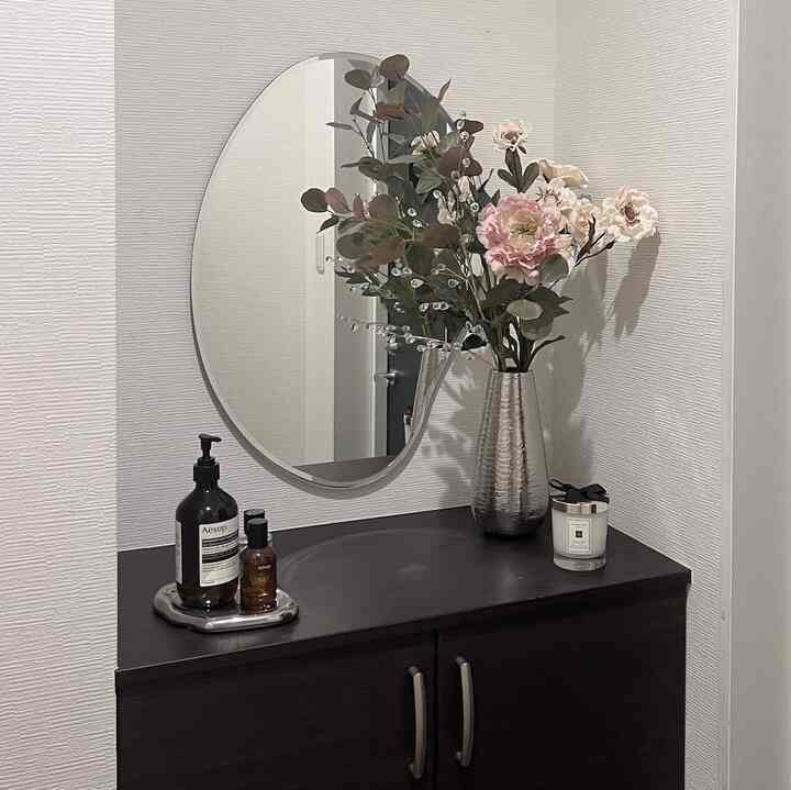 白いテクスチャ壁とダークブラウンのコンソールテーブルの上に花瓶と丸い鏡が配置された、シンプルでナチュラルな玄関のインテリア