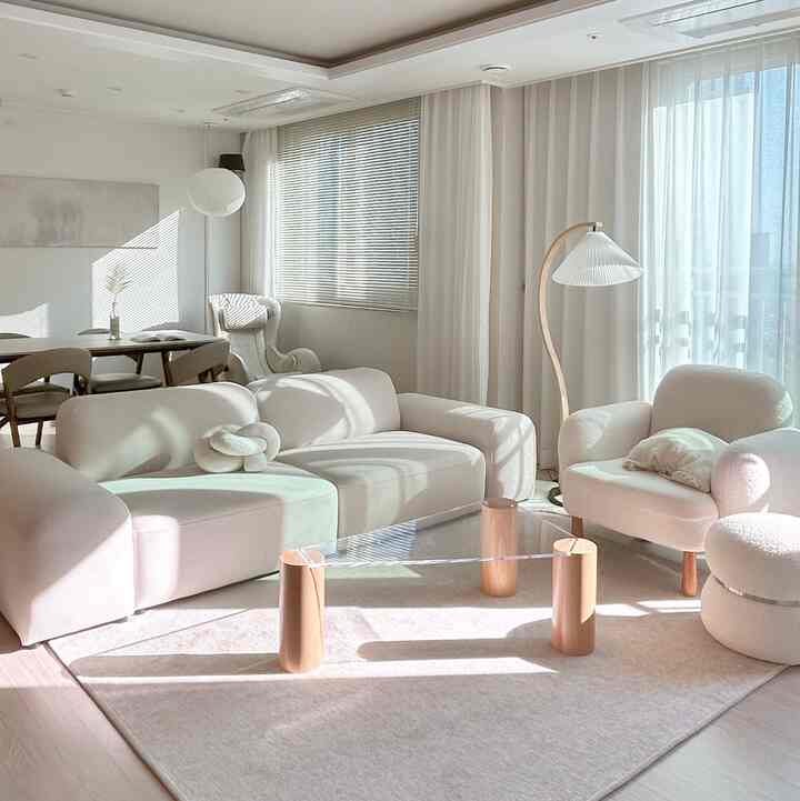 白と木目調が調和したミニマルでナチュラルモダンなリビング、柔らかなソファと透明なコーヒーテーブルが配置された温かみのある空間