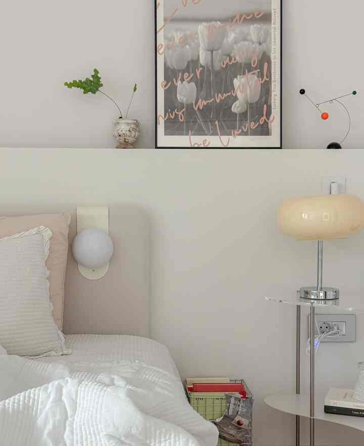 White and beige toned bedroom with picture frame above bed, lighting fixtures, and a side table creating a cozy atmosphere