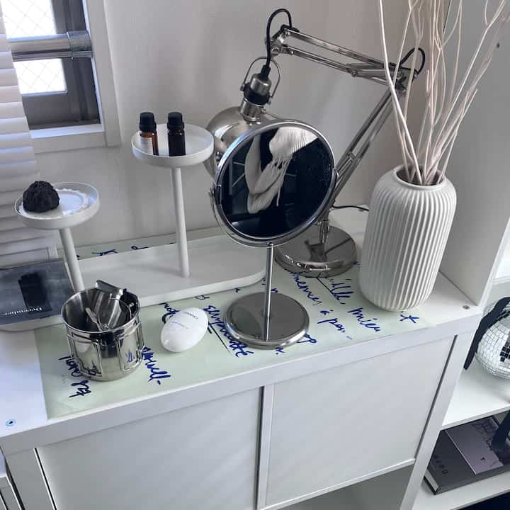 Simple vanity area in white and silver tones featuring a central mirror, lighting, and aroma items with a clean aesthetic