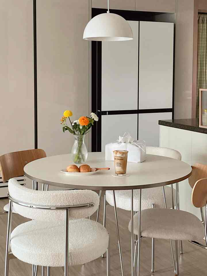 ホワイトとナチュラルトーンのキッチンスペース、シルバーフレームのブークレチェアと円形ダイニングテーブルが配置された雰囲気のあるおうちカフェ風インテリア